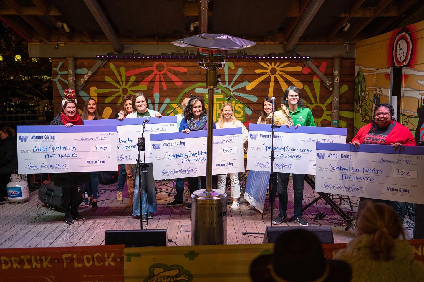 A group of individuals holding large checks on a stage.