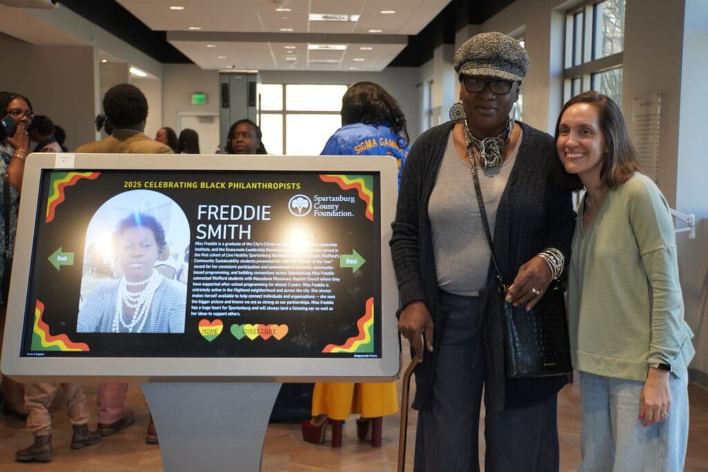 Two women standing beside a digital screen
